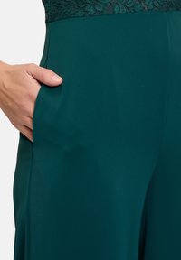 Groene wijde broek met een gladde stofstructuur, voorzien van een kanten tailleband en een zijzak die wordt benadrukt door handplaatsing.