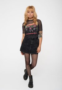 Black sheer T-shirt with graphic print, paired with a high-waisted black denim skirt. Black opaque tights and chunky black boots complete the outfit.