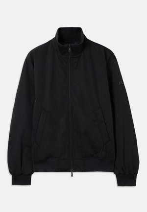 Chaqueta negra con cuello alto, cremallera frontal, dos bolsillos laterales, puños y dobladillo acanalados, hecha de material suave. Diseño sencillo, sin logotipos visibles.