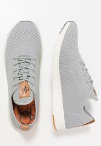 Sneakers in tessuto grigio con tomaia in maglia, suola bianca e dettagli in pelle marrone. Presentano un motivo testurizzato e un design con lacci.