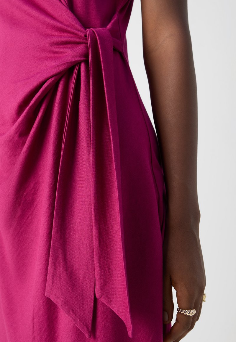 Fuchsia Kleid mit seitlichem Knoten, aus weichem Baumwollstoff und sanften Drapierungen. Die Textur ist glatt und hat eine fließende Silhouette.