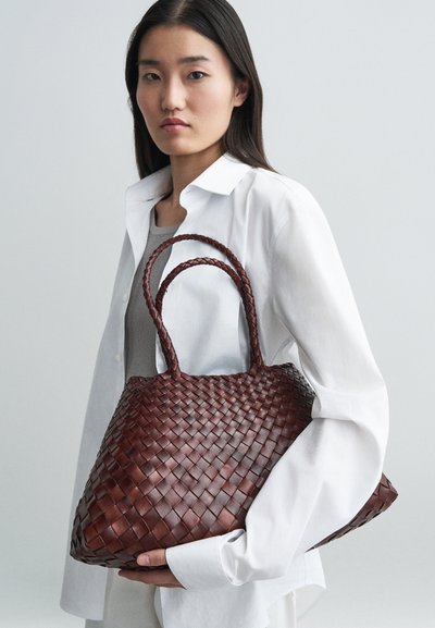 Καφέ υφαντή δερμάτινη τσάντα με διπλές λαβές, κωνικό σχήμα και υφασμάτινη επιφάνεια, φορεμένη με λευκό πουκάμισο και γκρι τοπ.