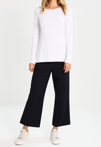 Maglietta bianca a maniche lunghe abbinata a pantaloni larghi blu navy e sneakers bianche. Il tessuto appare morbido con una vestibilità comoda e un design semplice.