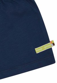 Beanie in cotone di colore blu navy con una texture morbida. Presenta un piccolo etichetta rettangolare con la scritta "loud + proud" in verde e accenti colorati.