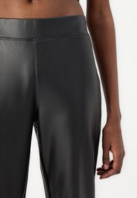 Black faux leather leggings with a smooth texture, high waist, and minimalistic design. Features a clean seam along the side.