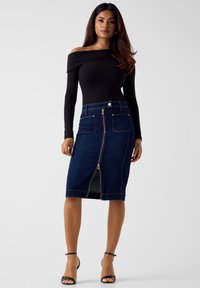 Jeans-Bleistiftrock mit einem Reißverschluss vorne, zwei Vordertaschen, dunkelblauer Farbe und kontrastierenden Nähten. Kombiniert mit einem schwarzen, schulterfreien Oberteil.