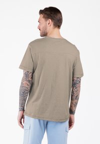 Khaki t-shirt z krótkim rękawem w miękkim materiale o luźnym kroju, z prostym dołem i detalem przy plecach.