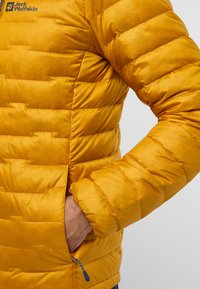 Veste isolante jaune avec un design matelassé, des poches latérales et une tirette de zip. Le matériau semble lisse avec une légère brillance.