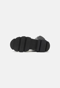 Suola di scarpa in gomma nera con un design testurizzato e segmentato, caratterizzato da ampie costole e bordi arrotondati per una maggiore aderenza e durata.