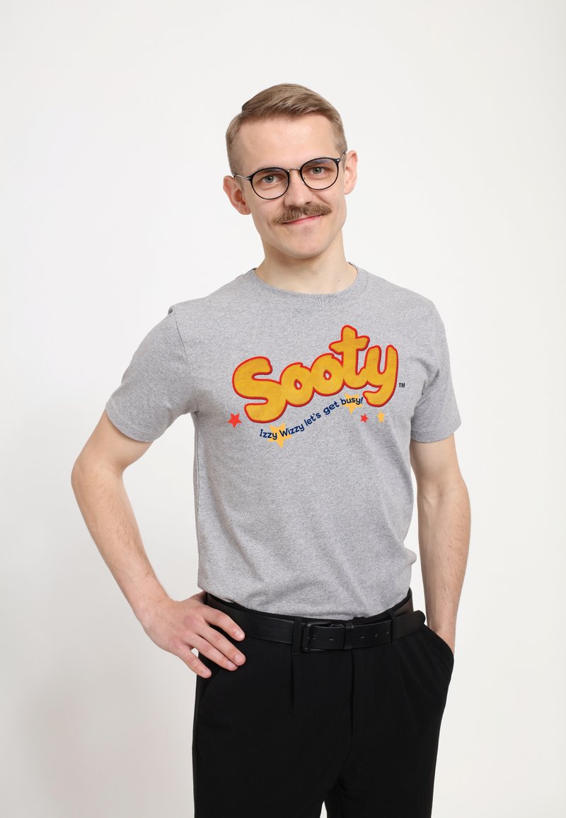Grå T-shirt med rund halsudskæring, der har fed gul "Sooty" tekst og blå stjerner. Sammen med sorte bukser og et sort bælte.