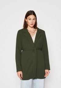 Olive green wrap coat with long sleeves, featuring a belted waist, notch collar, and soft texture. Worn over a light top and denim.
