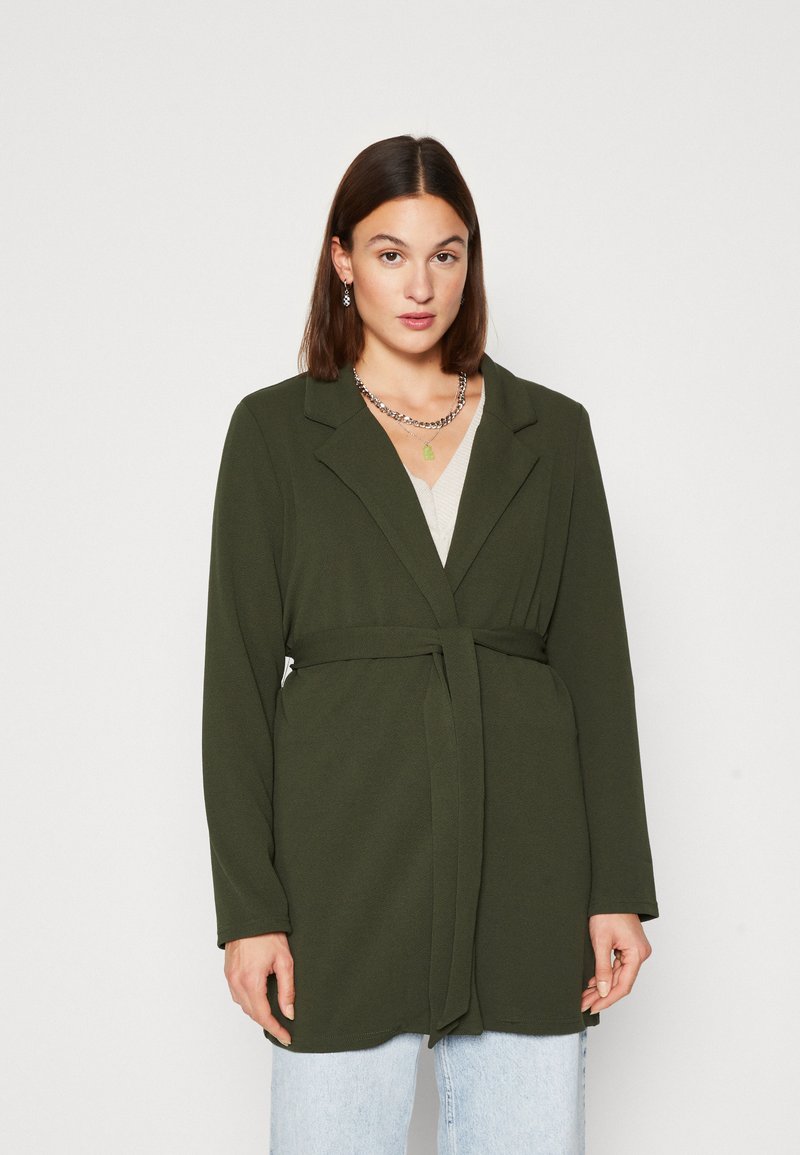 Olive green wrap coat with long sleeves, featuring a belted waist, notch collar, and soft texture. Worn over a light top and denim.