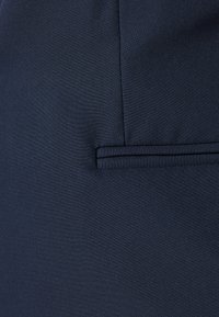 Tissu bleu marine présentant une texture lisse avec un design de poche plate et des détails de couture minimaux. Le matériau a un subtil éclat.