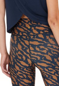 Marineblaue Sportoberteil mit drapierter Rückseite, kombiniert mit enganliegenden Leggings im Tigermuster in Braun und Marineblau, die die Textur betonen.