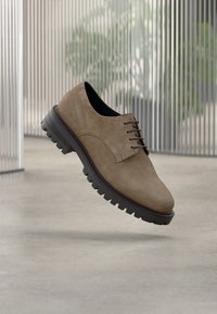 Ταμπά δερμάτινο παπούτσι από σουέντ με στρογγυλεμένη μύτη, διαθέτει παραδοσιακό σχέδιο με κορδόνια και ανθεκτική μαύρη λαστιχένια σόλα. Πλέει πάνω από μια λεία επιφάνεια.