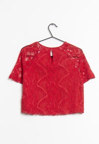 Blusa rossa in pizzo con maniche corte, caratterizzata da un design con apertura a chiave sulla schiena e da intricati motivi floreali. Texture morbida con un aspetto semi-trasparente.