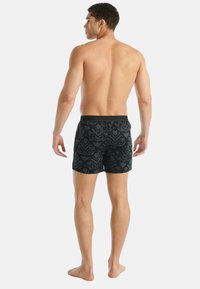 Černé plavecké kraťasy s květinovým vzorem, s jednobarevným páskem, navržené pro přiléhavý vzhled, hladkou texturou a délkou do poloviny stehen.