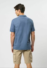 Gaiši zila polo krekls ar īsām piedurknēm, teksturēta auduma un brīvas piegriezuma, kombinēts ar bēšiem kravas šortiem ar sānu kabatām.