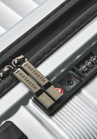Maleta dura plateada con tiradores de cremallera negra etiquetados como "pactastic" y un candado TSA establecido en 000.