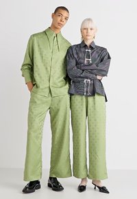 Zeleni satenasti komplet s suptilnim uzorkom, koji se sastoji od košulje dugih rukava s ovratnikom i hlača širokih nogavica; kombiniran s crnom prugastom bluzom i hlačama.