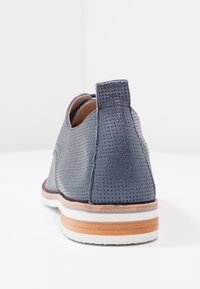 Scarpa in pelle perforata blu navy con punta arrotondata, suola in contrasto di colore tan e bianco, e tacco basso. Presenta una linguetta sul retro.