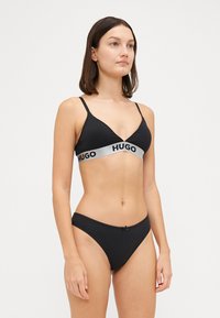 Μαύρο σετ μπικίνι που διαθέτει τριγωνικό τοπ με ασημένια λογοτύπηση και αντίστοιχα εσώρουχα μπικίνι με διακοσμητική κορδελίτσα. Απαλή υφή υφάσματος.