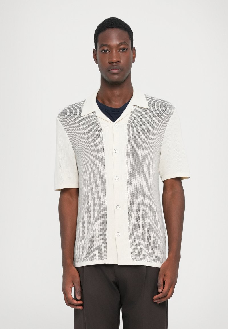 Short-sleeve, two-tone button-up shirt in cream and light gray. Features a textured design with a collar and five buttons down the front.