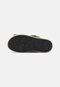 Suola in gomma nera con un motivo di presa testurizzato e intersuola beige chiaro; presenta il marchio "Clarks Originals" impresso vicino al tallone.