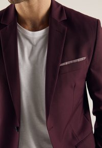 Burgundy blazer with a smooth texture, notch lapels, and a matching pocket square, worn over a white crew neck t-shirt.