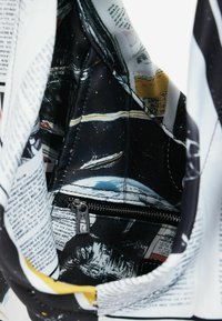 Koti koti puhul, millel on mustast kangast vooder kosmoseteemalise trükiga, lukuga tasku ja valgel taustal trükitud ajalehest stiilis tekst.