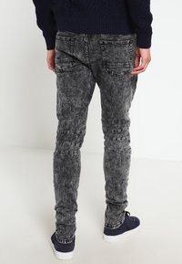 Wypłowiałe czarne dżinsy typu skinny z teksturowanym wykończeniem, pięcioma kieszeniami i widocznymi detalami ściegów, w połączeniu z niebieskimi trampkami.