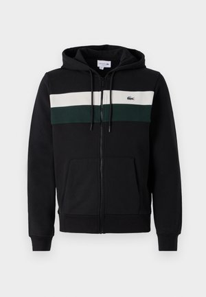 Black zip-up hoodie made of soft fabric. Features a white and dark green horizontal stripe across the chest and a front pocket. Hood included.