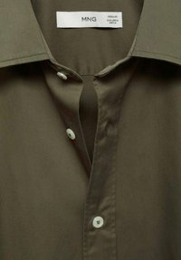 Olijfgroene shirt met een spitse kraag, voorzien van een voorflap met vier witte knopen en een gladde textuur. Merklabel zichtbaar aan de binnenkant.