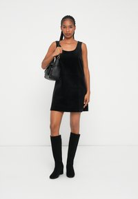 Rochie din catifea neagră fără mâneci, cu o croială dreaptă, asortată cu cizme negre până la genunchi și o geantă mică neagră. Textură fină.