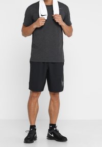 Camiseta y pantalones cortos deportivos Nike de color negro con un logo gris, combinados con zapatillas negras y una toalla blanca colgada alrededor del cuello.