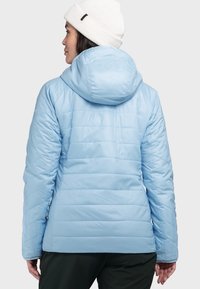 Hellblaue isolierte Jacke mit Kapuze, die ein gestepptes Design, eine glatte Textur und elastische Bündchen aufweist, kombiniert mit dunkelgrünen Hosen.