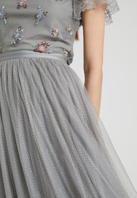 Graues Kleid mit bestickten Blumenmustern in verschiedenen Blau- und Rosatönen. Es hat einen durchsichtigen Stoff, eine gepunktete Textur und einen Satinalgürtel in der Taille.