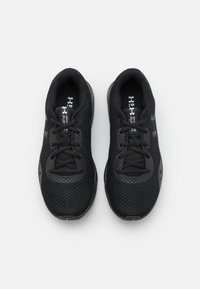 Scarpe da atletica nere con una tomaia in rete traspirante, punta arrotondata, superficie texturizzata e lacci piatta, che mostrano un design minimalista.