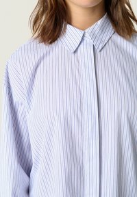 Light blue striped shirt featuring a classic collar, button front, and loose fit. The fabric has a smooth texture with thin vertical stripes.
