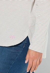 Maglietta a maniche lunghe a righe in crema e marrone, con un accento logo rosa sull'orlo, abbinata a jeans in denim blu scuro.