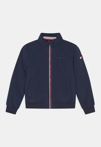 Granatowa kurtka z kołnierzem typu stójka, przednim zamkiem błyskawicznym i ściągaczami na mankietach. Posiada czerwone i białe akcenty na zamku i rękawie.