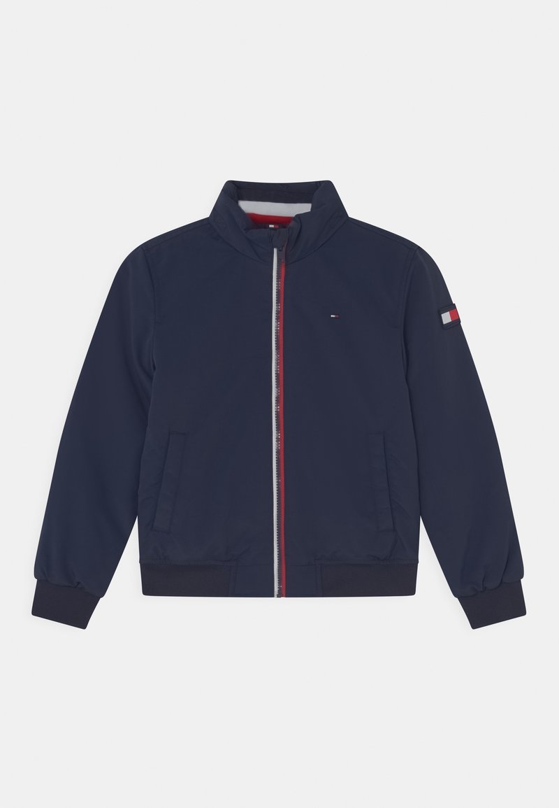 Granatowa kurtka z kołnierzem typu stójka, przednim zamkiem błyskawicznym i ściągaczami na mankietach. Posiada czerwone i białe akcenty na zamku i rękawie.