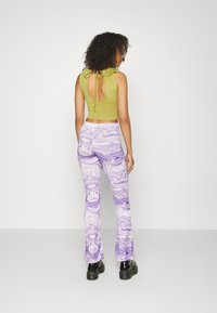 Top crop verde-oliva com detalhe de laço nas costas, combinado com calças flair em mármore roxo. O material parece suave com uma textura macia. Botas pretas.