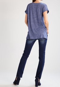 Blå t-shirt med uppvikt ärm, slits bak, och lös passform, kombinerad med mörkblå tajta jeans och kraftiga klackar.