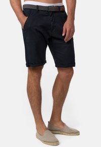 Shorts navy avec ourlets roulés, fabriqués en tissu léger. Présentent des poches latérales, une ceinture tissée grise avec une accent en cuir marron.