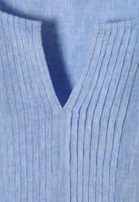 Top in lino azzurro chiaro con scollatura a V e pieghe verticali sul davanti, che mette in evidenza una texture liscia e una leggera lucentezza.
