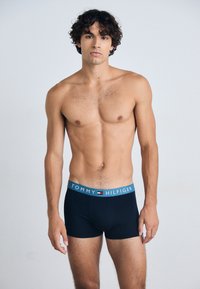 Boxers pour homme de couleur bleu marine avec une ceinture bleu clair arborant le logo "TOMMY HILFIGER". Tissu lisse, coupe ajustée et longueur jusqu'à mi-cuisse.