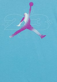 Camiseta de color azul claro con un gráfico de una figura en salto en rosa y blanco, con "23" y estrellas de fondo. Textura de tela suave.