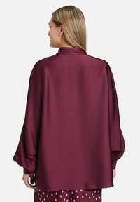 Maroon satin blouse with a loose fit, balloon sleeves, and a soft texture. Features a collar and falls to the hips, worn over a polka dot skirt.