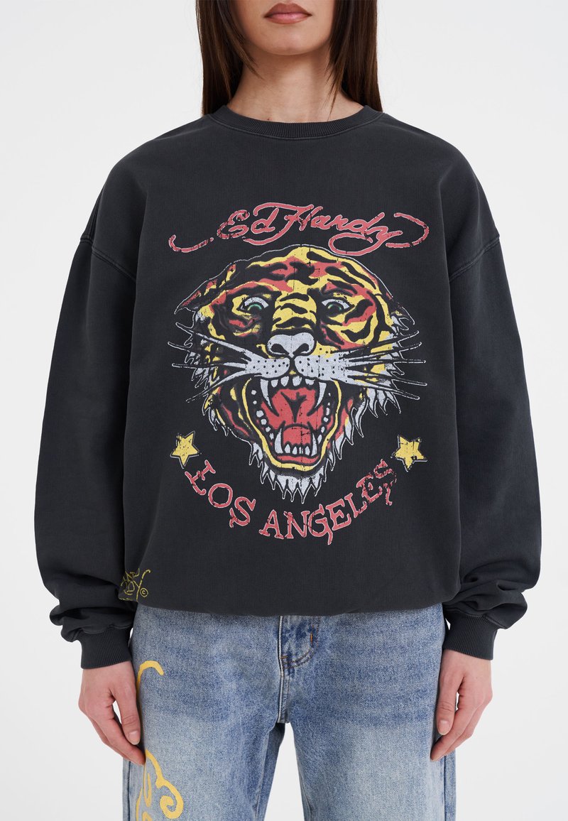 Zwarte sweatshirt met een kleurrijke tijgerafbeelding met gedurfde lijnen, "Ed Hardy" tekst en "Los Angeles" daaronder, tegen een losse pasvorm.